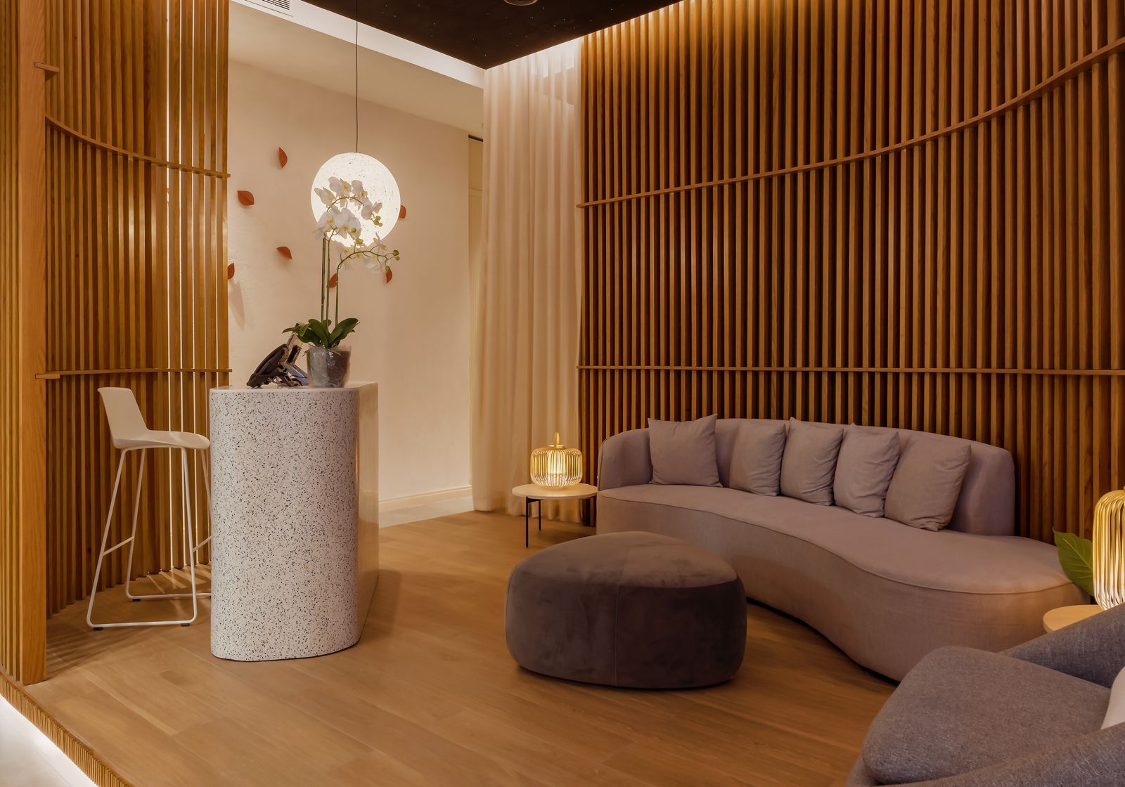 Terrazzo reception counter beside curved oak-slat walls and a lounge sofa